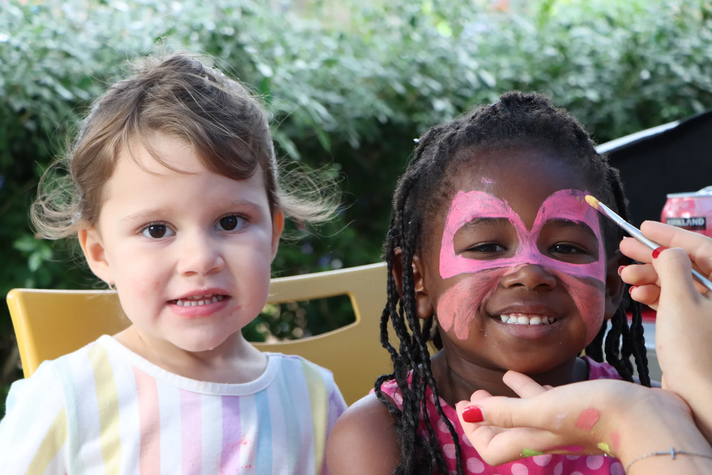 Two girls smiling at an outdoor Christchurch Kids event, one having a butterfly painted on her face