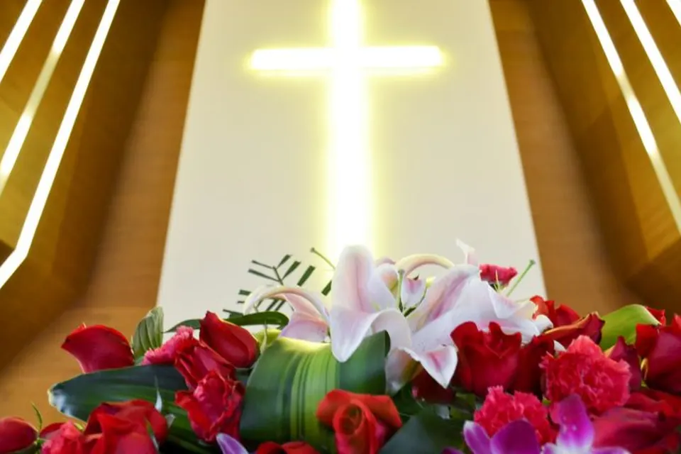 A lit cross above flowers at the front of a church