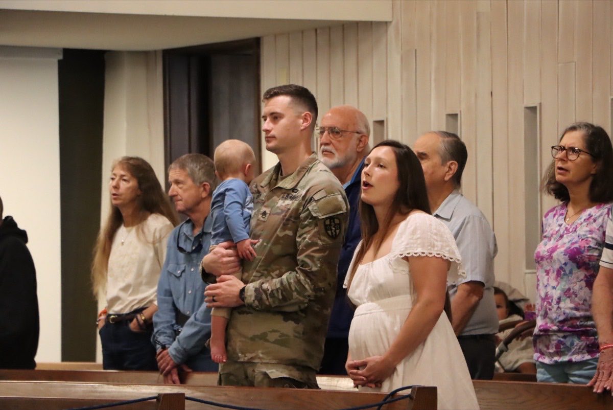 A family worshipping together, including a soldier holding a toddler