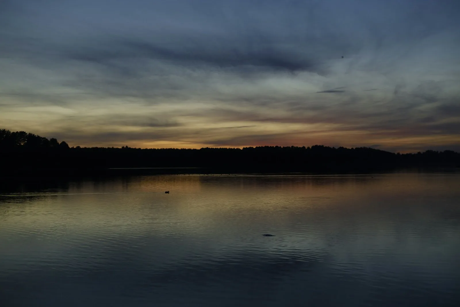 First light low on the horizon over a dark, calm lake.