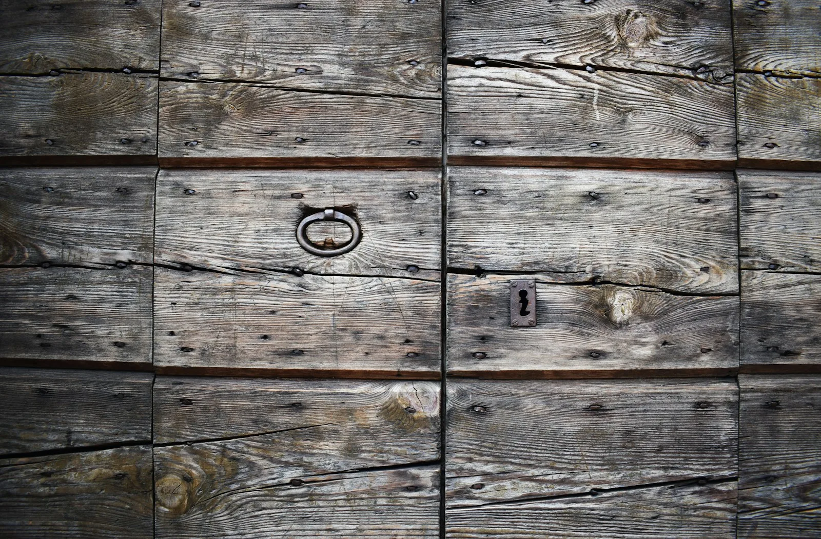 A weathered wooden door with an iron ring handle, shut.