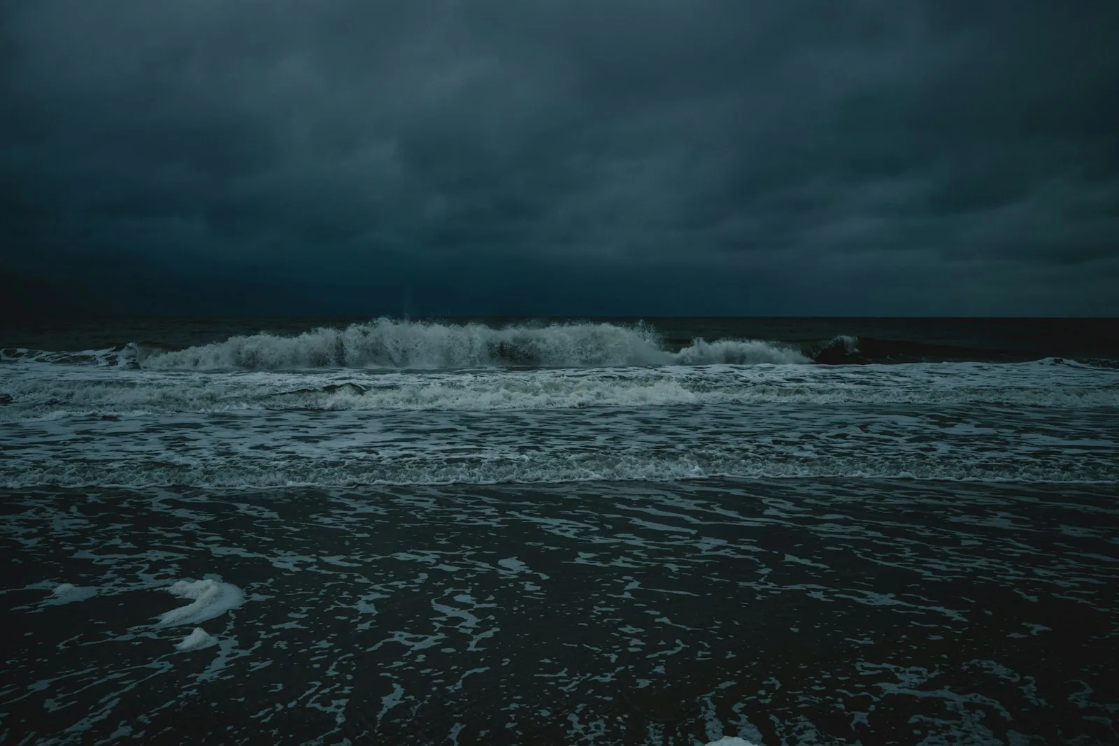 A dark ocean with waves crashing toward the shore under a heavy sky.